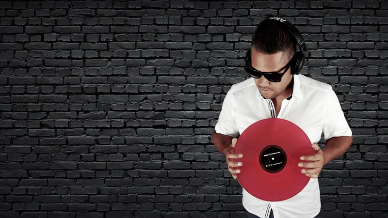 DJ Sammy mit Kopfhörern, Sonnenbrille und roter Schallplatte vor einer dunklen Backsteinwand