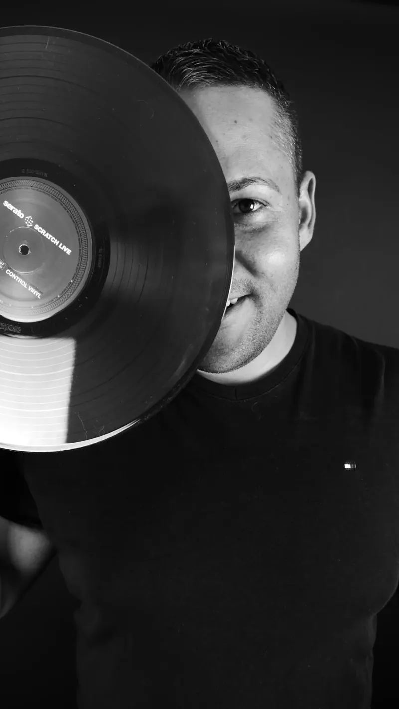 Schwarz-Weiß-Porträt von DJ Sammy mit einer Schallplatte vor einer Gesichtshälfte